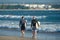 A pair of surfers walk with surfboards on a beach along a sea