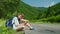 A pair of travelers with backpacks sits on the side of the road. They rest, they use a digital tablet