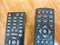 A pair of TV remotes laying next to each other. Two Television Remote Controls Side by Side on a Wooden Table. Partial