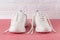 Pair of white chunky sole sneakers on a pink coral colored floor. New female or teen untied laces shoes for active lifestyle,