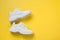 Pair of white female sneakers on yellow. Flat lay, top view minimal background
