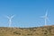 A pair of windmills on a clear blue sky in the Sierra del Merengue next to a meadow with cows in Plasencia.