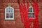 Pair of windows on brick wall straight on with one surrounded by vibrant red vines