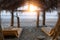 Pair of wooden sunbeds under a canopy of cane roof on the beach at sunset