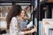 Pair of young beautiful girls in casual stylish clothes standing near bookshelves in library, looking at each other