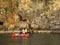 A pair of young people in sports clothes row around the rocks lit by sunlight on a rubber inflatable boat of red color. Peering cl