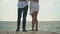 Pairs of slender legs of a young hugging guy and girl on the beach of ocean in windy but warm weather. Slow motion.