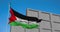 Palestinian flag waving on a flagpole with a concrete wall rising up behind.