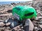 Palm-frond-green buoy washed up on beach of white rocks