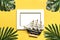 Palm and monstera leaves, orchid, seashells, white photo frame, ship on a yellow background.