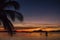 Palm tree and boats silhouettes on bright sunset sky background. Scenic sunset on tropical beach with mountains on background.