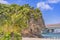 Palm tree on the sandy beach Naminoue topped by a huge rock with a Shinto Shrine at the top of a cliff and a highway passing in