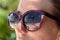 Palm tree, white beach and crystal clear blue water reflected in the sunglasses of a woman. Maldives