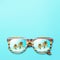 Palm trees and mountains are reflected in sunglasses with a multi-colored wooden frame on a blue background, top view