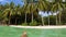 Palm Trees On Sandy Ocean Beach With Turquoise Water In Kaimana Island, Raja Ampat. Man Swimming In Sea And Enjoys