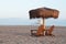 A palm umbrella stand above wooden adirondack chairs on a Pacific ocean beach