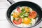 Pan of fried eggs with tomatoes, cheese, spring onion, herbs on a white table. White wooden table. Concept of food. Breakfast time