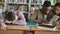 Pan shot of diligent students preparing for exams doing homework and tired guy sleeping on table in college library