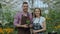 Pan shot of young smiling blogger couple gardeners in apron holding flower talking and recording video blog for online