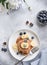 Pancakes with fresh blueberries, banana on a gray background with white flowers.