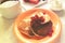 Pancakes in orange plate and glass of sourcream with red berries, slice of watermelon, wooden table and white cloth.