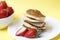 Pancakes on a plate and strawberries on a yellow background, front view