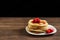 Pancakes on a white plate with strawberries on a brown wooden background. Chef man hand. Beautiful food still life. Natural light