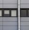 Panels on an industrial building with a row of back window frames and a silver pipe running up the wall