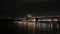 panning aerial footage of the San Francisco Oakland Bay Bridge with lights and ships sailing in the bay at night in San Francisco