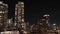 panning aerial footage of skyscrapers, hotels and office buildings in the city skyline at night and lush green trees