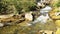 panning footage of the rushing water, rocks and waterfall at Anna Ruby Falls with lush green trees and plants in Helen Georgia