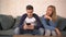 Panning shot young man using social media on mobile phone ignoring his girlfriend at home sofa couch with the woman frustrated