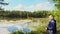 Panning view elderly blond caucasian woman stands holding red nordic sticks and enjoying lake