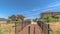 Pano Bridge over a grassy terrain with homes mountain and blue sky background