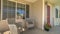 Pano frame Wicker armchairs on the sunlit front porch of home with brown front door