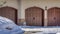 Pano Garage entrance with snowy driveway leading to three arched wooden garage doors