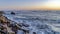 Pano Ocean waves crashing on jagged rocks with blue sky and golden sun at sunset