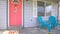 Pano Red front door of house with blue porch chairs against windows with shutters