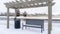 Pano Wooden pergola over bench and garbage can along a road on a snowy winter day