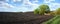 panoram of plowed field and green tree on the side spring time