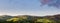 Panorama of beautiful green hills, mountains, and fields in sunset light under a blue sky with purple clouds