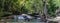 Panorama of a beautiful waterfall with a scrubby beach on the right in the dense forest of Erawan National park in Thailand