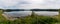 Panorama of a calm lake with reflections of mountains and sky and canoes and boat in the foreground