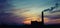 Panorama of city sunset and silhouettes of cranes, high-rise buildings and construction site with smoke