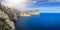 A panorama of the cliffs on the coastline of PollenÃ§a, Mallorca and a single white sailboat on the beautiful blue waters