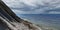 Panorama of a cloudy seascape. A picturesque stone wild beach at the foot of the rocks in rainy weather and a ship on the horizon