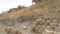 Panorama Damaged stone blocks retaining wall lining a hill with homes under cloudy sky