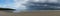 Panorama of an empty and large beautiful golden sand beach underneath a bad weather sky