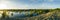 Panorama of evening landscape over flooded land next to a levee with sun setting to the left