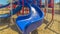 Panorama Focus on the bright blue slide at a park against houses and sky on a sunny day